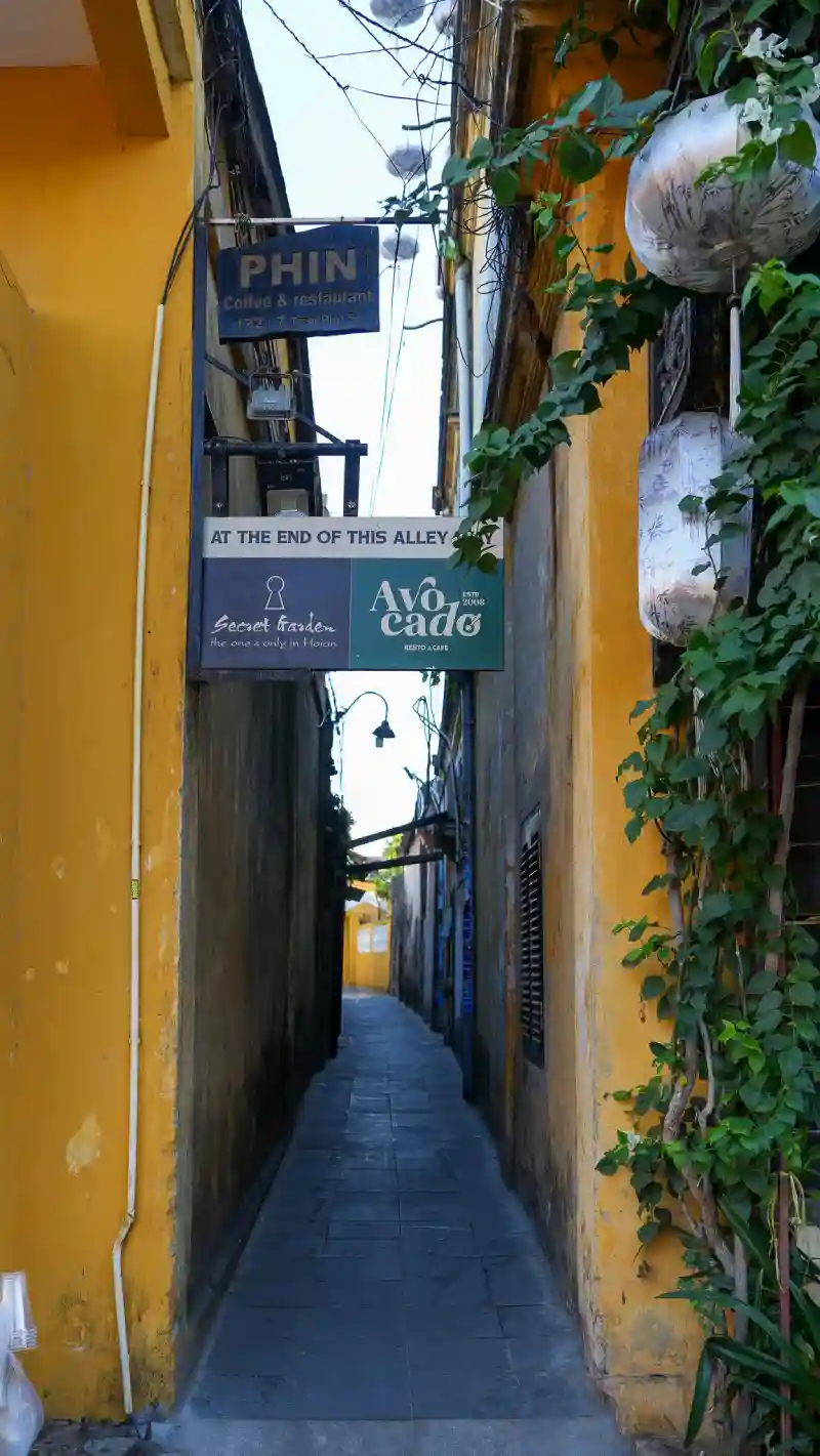 Narrow yellow-walled alley in Hoi An Ancient Town with lanterns and tailor shop signs