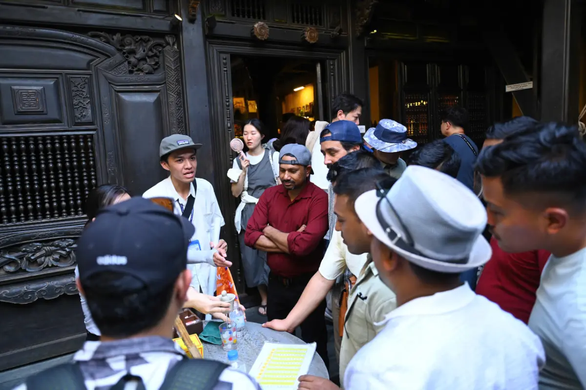 Free walking tour group listening to their local guide at the ornate wooden entrance of the Fujian Assembly Hall in Hoi An.